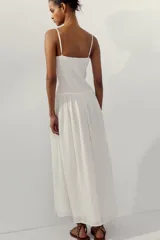 Vestido midi de color blanco con escote recto y tirantes finos ajustables. Presenta un cuerpo con tejido elástico tipo nido de abeja y detalles de flores bordadas en la parte superior. Cuenta con bolsillos laterales ocultos y forro interior.