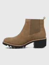 Bota tipo Chelsea de Hush Puppies, confeccionada en material sintético efecto gamuza color marrón. Presenta elásticos laterales al tono para facilitar el calce, suela robusta de goma negra con plataforma y taco ancho.