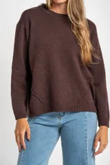 Sweater de tejido de punto liso, color marrón oscuro, con cuello redondo y calce oversize. Presenta detalles de costura en diagonal en la parte inferior delantera.