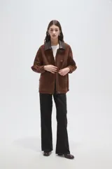 Chaqueta de gamuza color marrón con cuello camisero en cuero oscuro, cierre frontal con broches metálicos tipo gancho y bolsillos delanteros aplicados.