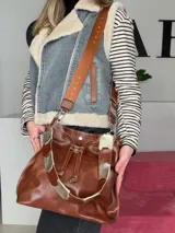 Bolso tipo bucket bag Chabas modelo 3.1, confeccionado en cuero genuino de color marrón. Cuenta con cierre de cordón ajustable, dos tipos de asas (una corta de cuero con detalles decorativos y otra larga tipo bandolera con tira textil) y diseño sin forro interior.