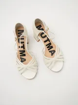 Sandalias de charol color blanco con múltiples tiras finas cruzadas en el empeine. Tienen pulsera con hebilla dorada y tacón cuadrado.