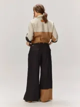 Pantalón sastrero de corte ancho, color beige con rayas verticales blancas y detalles de costuras pespunteadas.