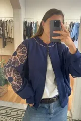 Campera bomber de jogging color marrón, con cierre frontal y bordados florales en las mangas.