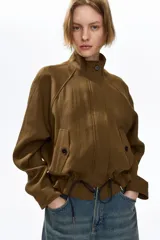 Campera corta verde militar en mezcla de lino, con cuello elevado, mangas raglán, bolsillos frontales con solapa y botones, y cordón ajustable en el bajo.