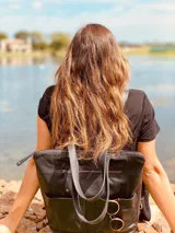 Mochila negra de cuero convertible en bolso de mano o bandolera. Tiene compartimento para laptop, bolsillos exteriores y correas ajustables y extraíbles.