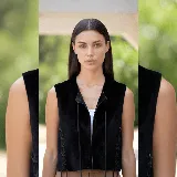 Chaleco negro de cuero, con diseño sin mangas y cierre frontal con tiras finas para anudar. Presenta detalles de cordones cruzados en los laterales, estilo corset.