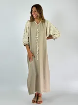 Vestido largo color beige con mangas tres cuartos de crochet y detalle de cordón con borlas en el escote.