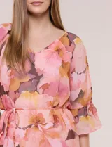 Vestido corto de gasa semitraslúcida con estampado floral en tonos rosados, naranjas y marrones. Posee escote en V, mangas tres cuartos acampanadas con abertura, y un fino lazo ajustable en la cintura. Incluye forro interior a tono.