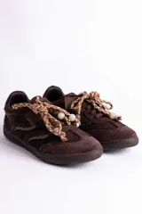 Zapatillas urbanas de gamuza color marrón, con diseño de cordones decorados con cuentas de piedra y detalles de líneas brillantes en los laterales. Presentan suela de goma texturizada al tono.