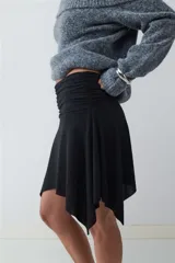 Minifalda negra de tiro medio con detalle de frunces en la cintura y bajo asimétrico con caída fluida.