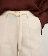 Bermuda de cintura mediana color beige, confeccionada en sarga, con trabillas, cierre tradicional, bolsillos y frisos delanteros. Incluye cinturón de tejido para lazo con hebilla metalizada.