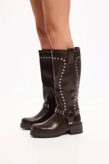 Bota de caña media en cuero sintético negro, con suela track, cierre lateral y detalle de tachas metálicas en la parte superior y en una tira decorativa sobre el tobillo.