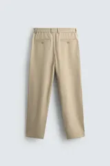 Pantalón de corte recto confeccionado en tejido elástico, con cintura elástica, pliegues frontales, bolsillos laterales y bolsillos traseros de vivo con botón.