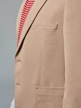 Saco color beige de piqué con cuello con solapas y bolsillos de plastrón. Mangas con coderas y bajo con abertura en espalda.