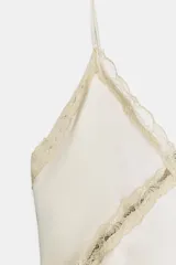 Top de satén color beige con escote en pico, tirantes finos y detalles de encaje aplicado en los bordes y formando una cruz en el frente.