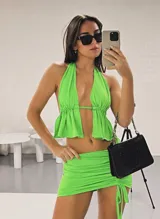 Conjunto de dos piezas compuesto por un top halter con volados y una minifalda ajustada con frunces laterales y tiras regulables.