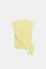 Top de popelín color amarillo claro, sin mangas, con hombreras marcadas, cuello alto y drapeado frontal con lazada lateral en la cintura.