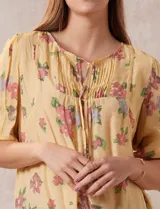 Blusa de gasa estampada con cuello a la base, escote en V plisado y lazo de ajuste. Delantera con detalles en puntilla y manga corta con puño fruncido.