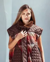Chaleco sin mangas de diseño híbrido que combina paneles de tela acolchada capitoné en color azul marino con secciones de tejido de lana a cuadros en tonos naranja, gris y negro. Presenta cuello con forro de piel sintética marrón, cierre frontal con cremallera y ribetes en color rojo vibrante. Incluye bolsillos delanteros amplios con cierre.