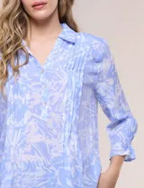 Blusa celeste con estampado efecto pincelada blanca, de corte semi holgado, escote en V con cuello solapa y media abotonadura frontal con botones nacarados. Presenta finas alforzas verticales en la pechera y mangas 3/4 con puños elastizados.