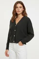 Cardigan de punto color negro, con cuello en V, cierre frontal con botones y bolsillos delanteros. Presenta un diseño de corte ajustado al cuerpo y mangas largas con puños acanalados.