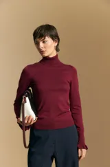 Polera de tejido fino color negro, con cuello alto y mangas largas con terminación sutilmente fruncida. Diseño ajustado al cuerpo.