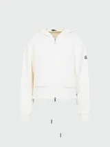 Cardigan de punto color blanco con capucha y cierre frontal de cremallera. Presenta dos bolsillos frontales con textura acanalada, puños elásticos y el parche del logo de Moncler en la manga.