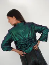 Camisa negra de satén con brillo satinado, escote en V, mangas largas y botones de nácar. Cuenta con cordones laterales ajustables para fruncir la prenda.