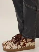 Championes urbanos con diseño de animal print tipo vaca en tonos marrón y blanco. Presentan cordones marrones, detalles en cuero marrón en el talón y suela de goma plana al tono.