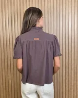 Camisa de manga corta color beige, con cuello alto con volados, botonadura frontal y mangas abullonadas con terminación fruncida.
