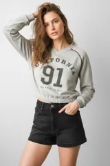 Buzo de algodón color gris melange, con cuello en V, mangas largas y diseño corto con ruedo elástico. Presenta una estampa frontal con la inscripción California 91 Los Angeles City.