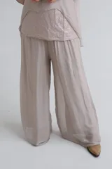 Pantalon de corte palazzo, confeccionado en tela semitransparente de textura fluida, color beige, con cintura elástica.