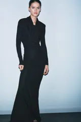 Vestido largo negro de manga larga confeccionado en mezcla de viscosa. Presenta cuello amplio multiposición y detalle de drapeado fruncido en el lateral del torso.
