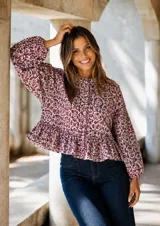 Camisa de lino con estampado geométrico en tonos bordó sobre base natural. Presenta cuello con volado, botones forrados al tono, mangas amplias con puños elásticos y un corte con volado en la cintura que aporta movimiento.