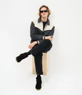 Campera de estilo varsity confeccionada en polyvelour, con diseño bicolor en gris oscuro y crema. Presenta cuello tipo polo, cierre frontal con botones a presión, mangas largas y puños y cintura con terminación en ribana a rayas.