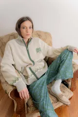 Saco de punto tipo cárdigan con cierre frontal, cuello alto y diseño jacquard con motivos geométricos y de paisaje. Presenta bordado en el pecho y cierre de aluminio.