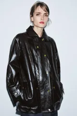 Chaqueta de efecto cuero color marrón oscuro con acabado brillante, cuello de solapa con aplicación de pelo sintético extraíble, manga larga con trabillas, bolsillos frontales de plastrón con solapa y cierre frontal con cremallera y botones a presión.