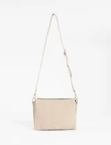 Bandolera de tamaño compacto en color beige, confeccionada en cuero vegano. Presenta un diseño con pespuntes verticales visibles, cierre superior y correa larga ajustable y extraíble. Incluye un pequeño aplique metálico decorativo en la parte inferior frontal.
