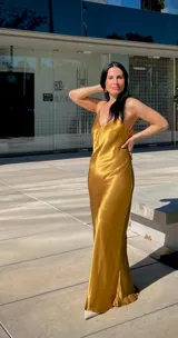 Vestido largo tipo slip dress de satén dorado, con escote en V, breteles finos y corte al bies que se ajusta suavemente a la figura.