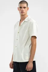 Camisa de manga corta color crema, con cuello camp y calce relajado. Confeccionada en mezcla de algodón y lino, con botones de coco con logo y parche característico de Polonio.