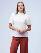 Blusa de cuello alto con torso en tejido crepe liso y mangas cortas abullonadas confeccionadas en encaje floral. Presenta un diseño elegante y versátil.