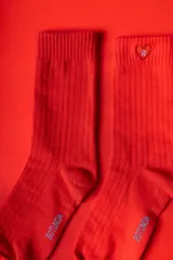 Medias de punto acanalado en color rojo intenso, con puño elástico. Presentan un detalle de corazón bordado con la letra R en la parte superior y el logo de la marca en la planta del pie.