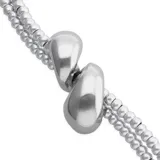 Pulsera de aleación de metales bañados en plata, compuesta por dos tiras de cuentas metálicas y detalles de cuero marrón oscuro, con un adorno central de dos gotas plateadas.