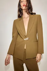 Blazer entallada color tostado con cuello solapa, manga larga y hombreras. Presenta cierre frontal con un botón metálico dorado y bolsillos delanteros de vivo.
