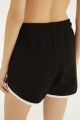 Short deportivo negro con ribetes blancos en los bordes y las aberturas laterales, con cordón ajustable en la cintura y estampa con la palabra "RIO" y un huevo frito en la pierna derecha.