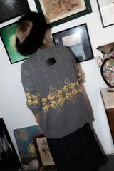 Saco de punto gris con diseño geométrico en color amarillo, cierre frontal con botones, cuello redondo y bordado de corazón pequeño en el pecho.