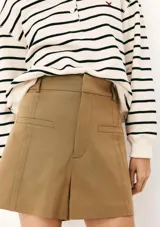 Short de sastre color beige, de tiro alto, con bolsillos laterales tipo ojal y costuras verticales decorativas en el frente.