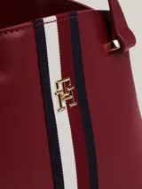 Cartera tote Tommy Hilfiger color borgoña, con doble asa corta y correa larga extraíble. Presenta una franja vertical con los colores de la marca y el logo TH dorado.