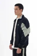 Campera negra de nylon con recortes en forma de V en color gris en las mangas. Tiene cuello mao, cierre frontal, puños y cintura elásticos, bolsillos laterales y logo estampado en el pecho y en la manga izquierda.